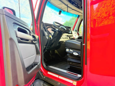 Kenworth T680 cab interior view from open driver door showing steering wheel and dashboard.