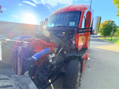 Truck engine bay of a red 2025 Kenworth T680 with hood open, showing turbo pipework and engine components.