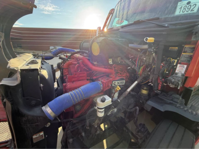 Kenworth T680 engine bay with red engine, blue hoses, white reservoir, and various labels visible.