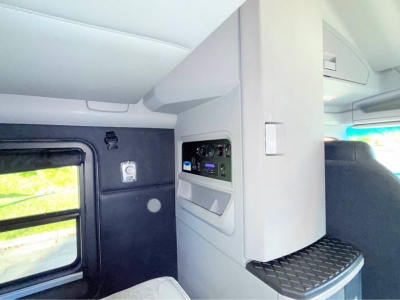 Cab interior of a Kenworth truck showing control panel, shelves, and seating area in a sleeper cab.