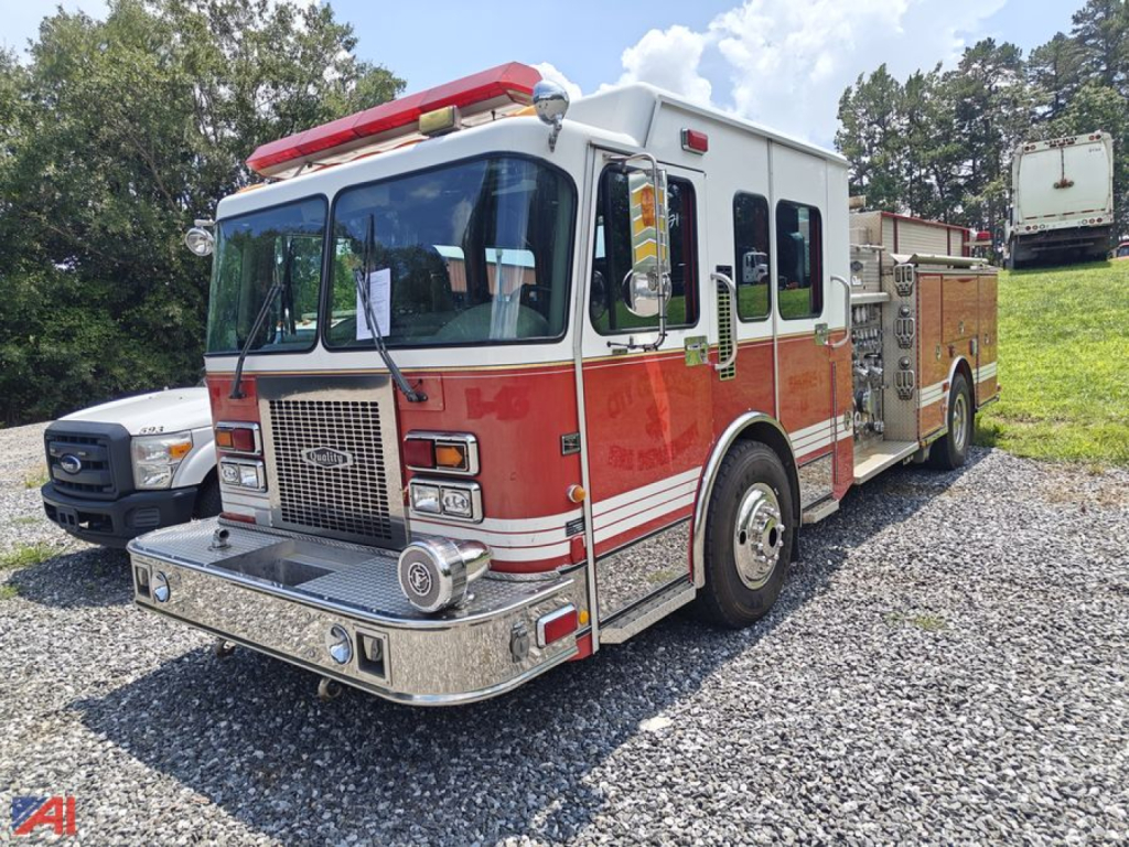 Fire truck with red and white livery parked on gravel; front grille, lights, and equipment compartments visible.