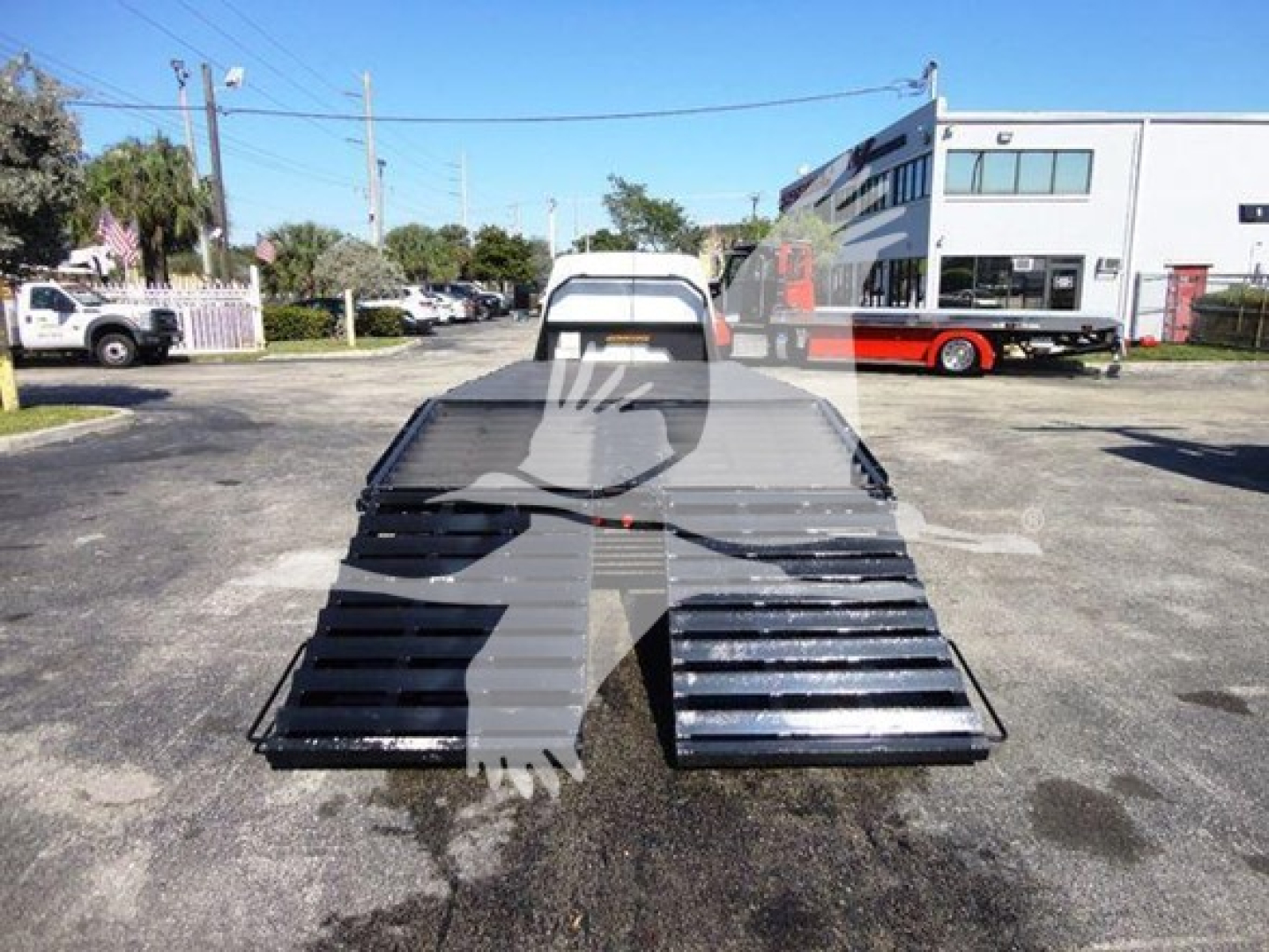 Flatbed tow truck bed from rear view with steel planks and ramps on either side, Ford E450 work truck in background