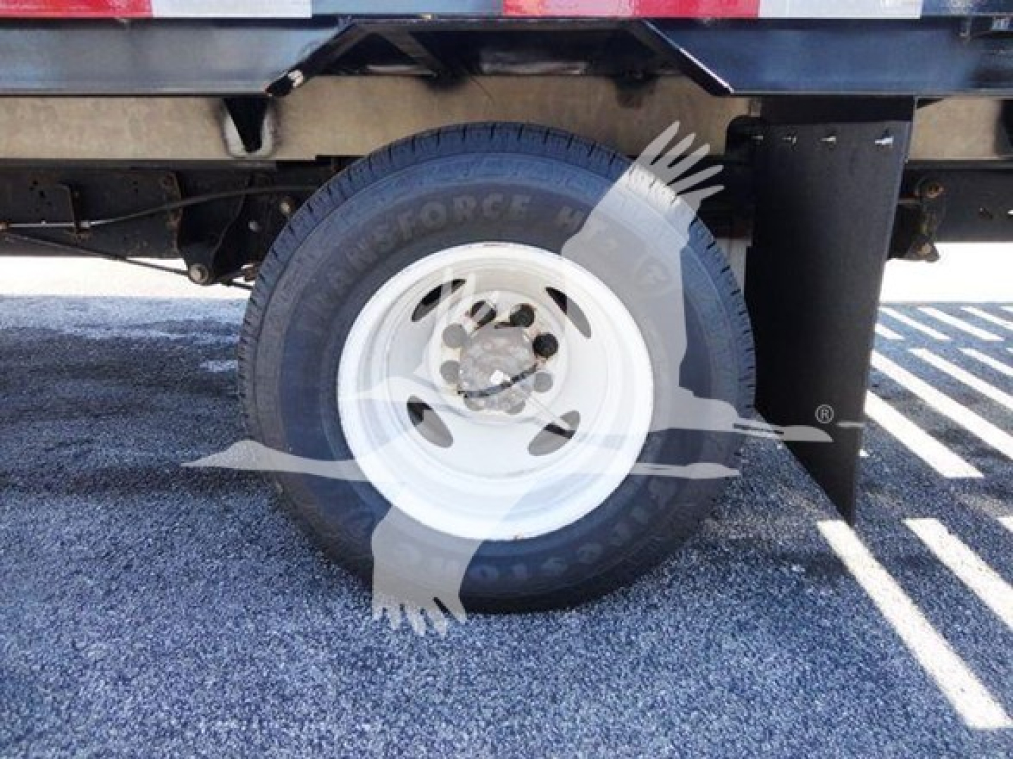Flatbed truck rear wheel assembly showing white steel wheel and black tire with Ford van axle and suspension components visible.