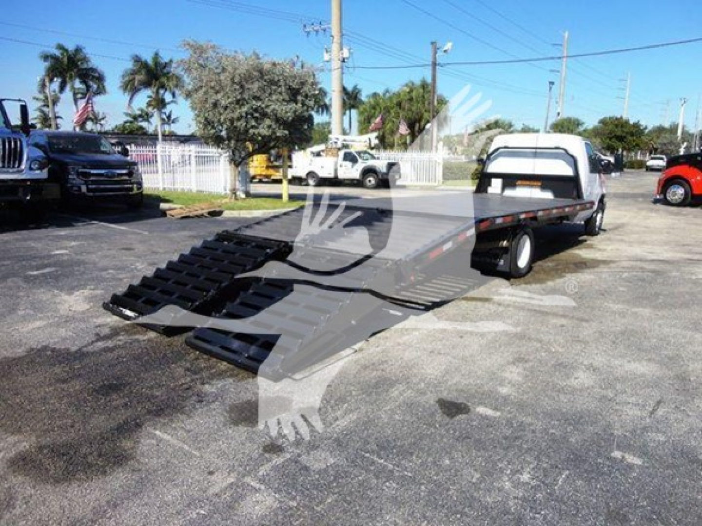 Flatbed tow truck with a gooseneck wheel-lift in a parking lot, Ford E-450 chassis cab, black ramps extended on flatbed.