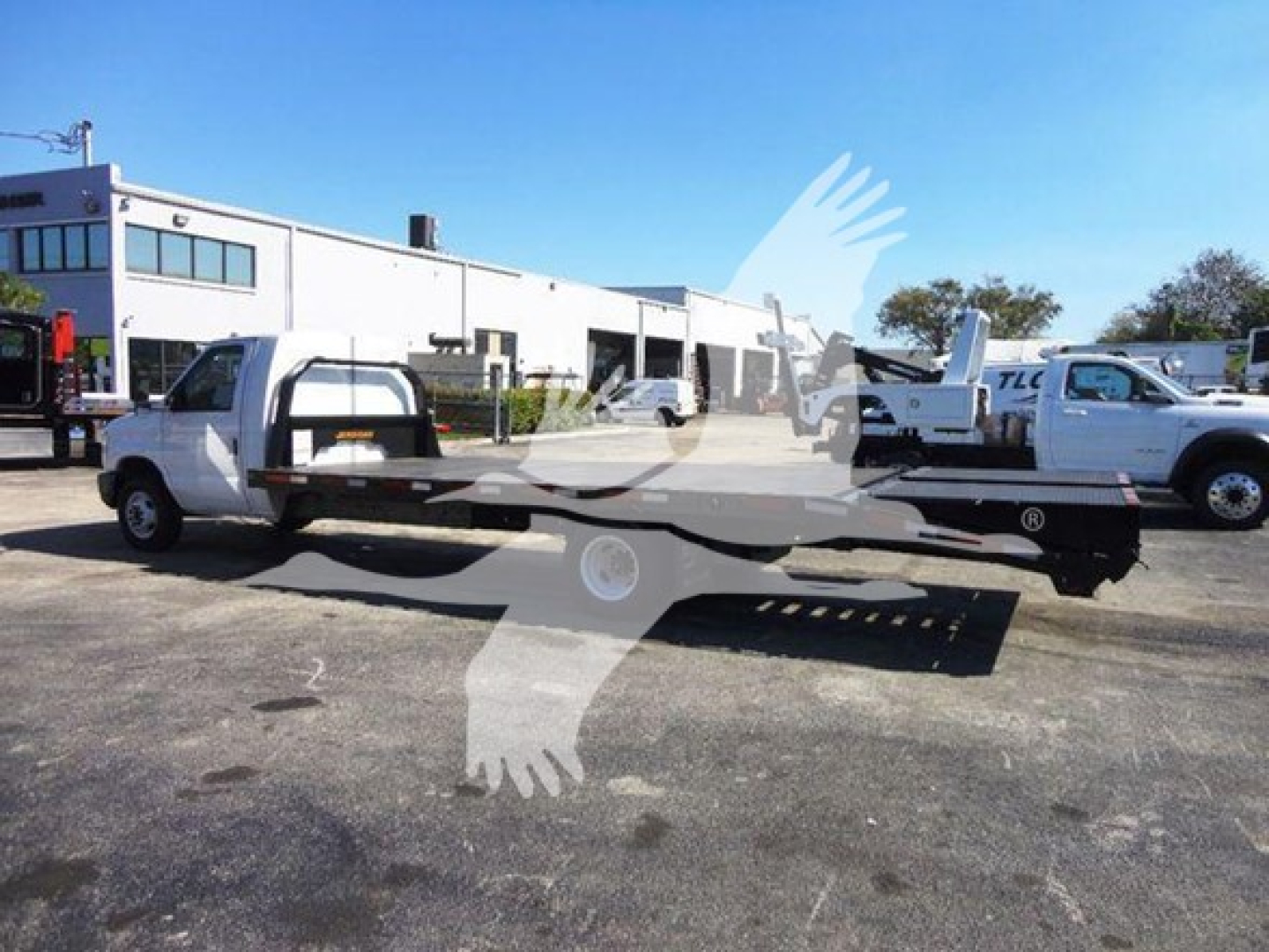 Flatbed tow truck chassis with white cab and flatbed, side view.
