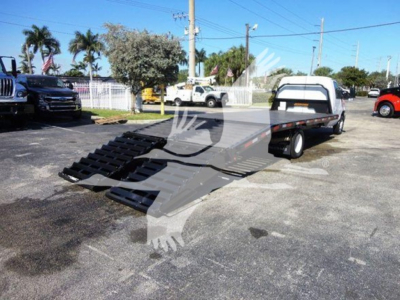 Flatbed tow truck with a gooseneck wheel-lift in a parking lot, Ford E-450 chassis cab, black ramps extended on flatbed.