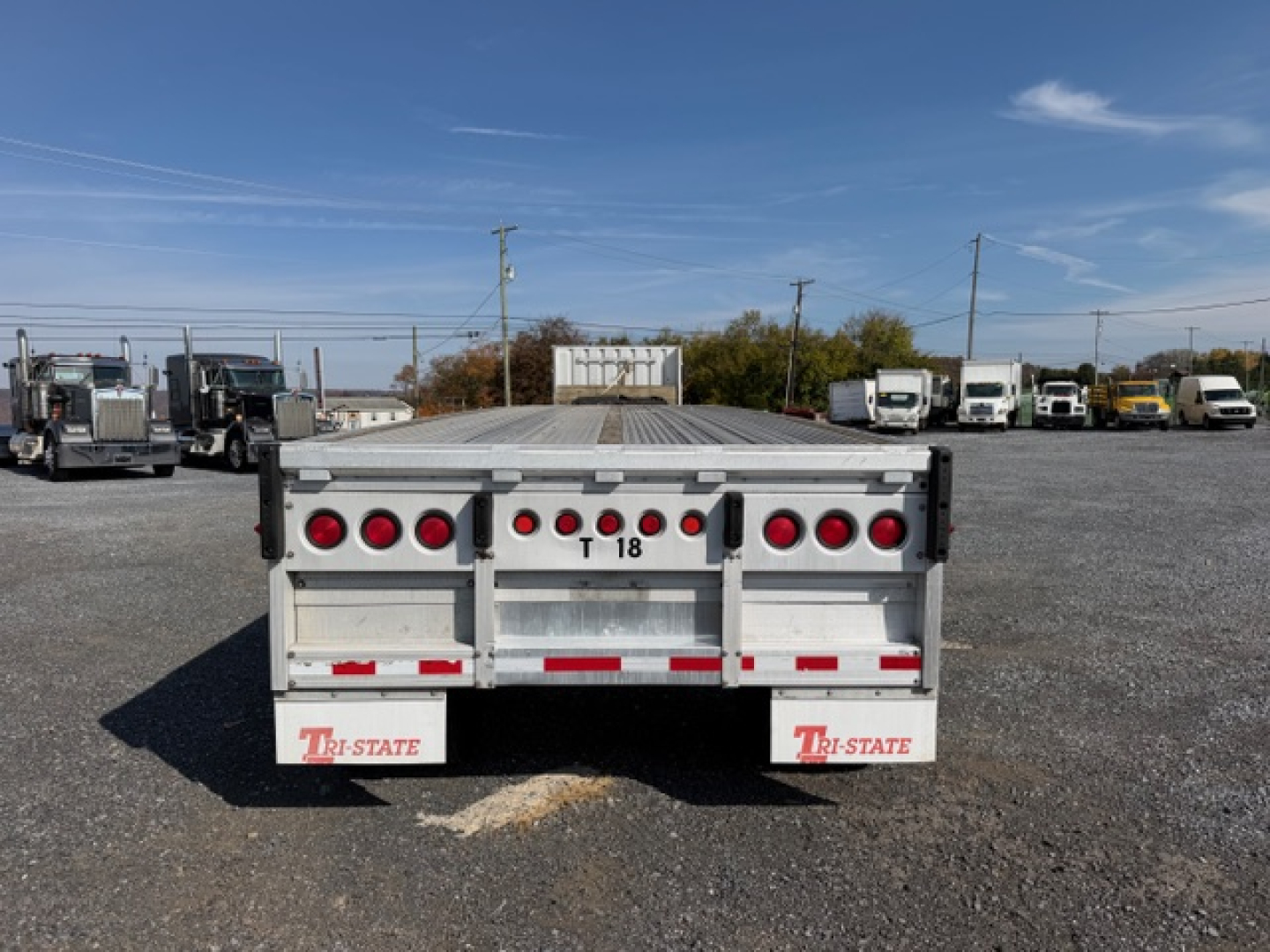 Flatbed trailer rear showing taillights, bumper, and 'TRI-STATE' mudflaps. Plateless center, T18 marking, and reflector strips.