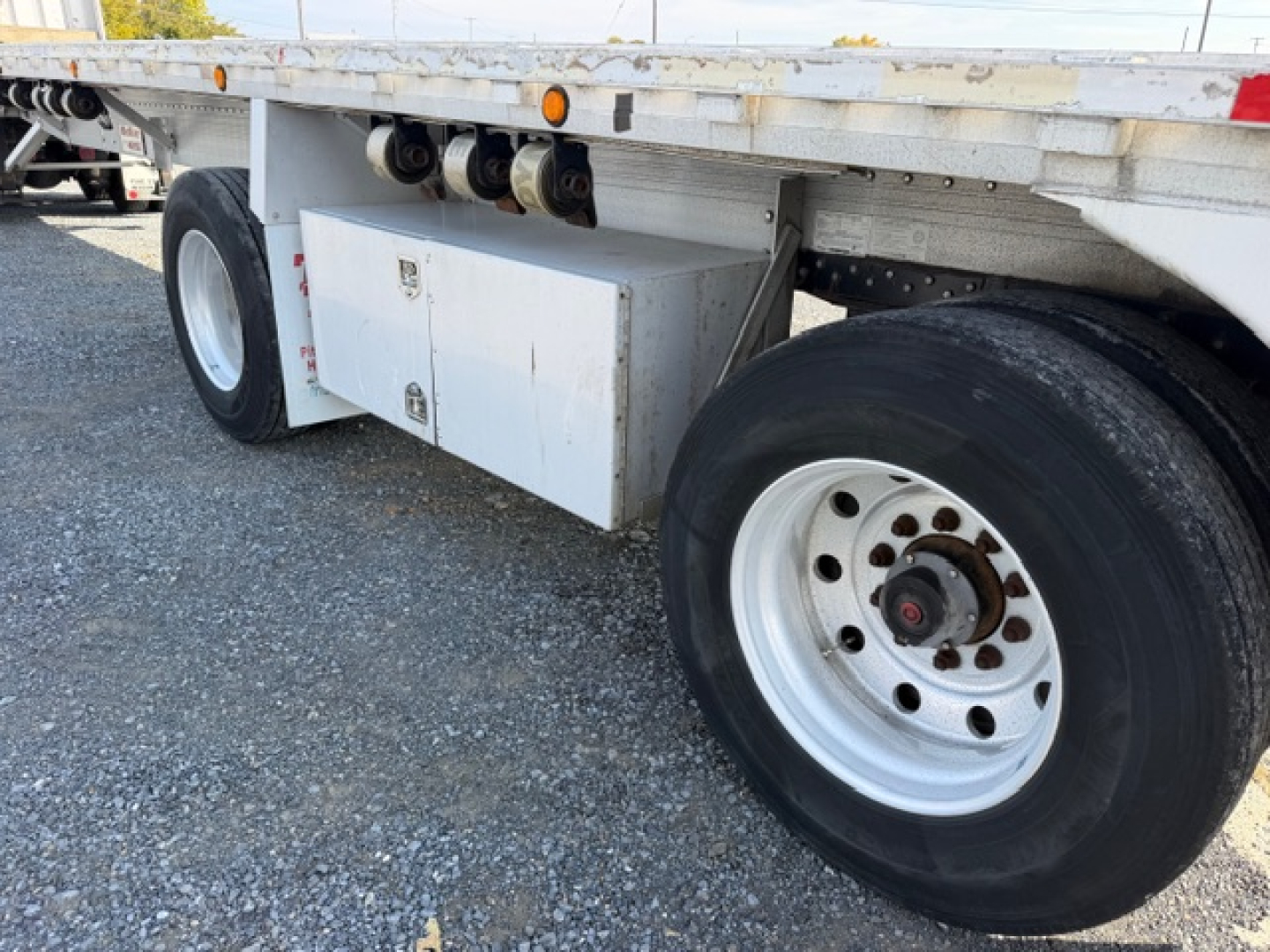 Flatbed trailer wheel area showing dual rear axle, white storage box, and chrome18.5 inch rims on a 2004 Reitnouer MaxMiser 45x96 trailer.