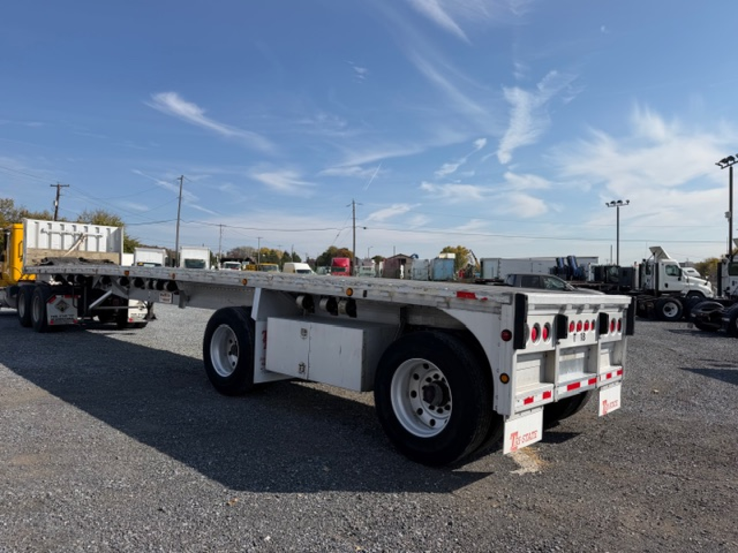 Trailer in a lot showing flatbed with dual rear axles, white sides, storage boxes, and Ramp/kingpins area visible.