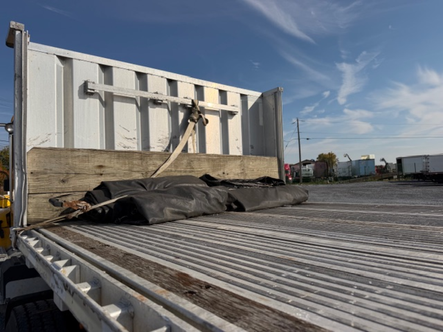 Trailer bed and rear wall of a 2004 Reitnouer MaxMiser flatbed trailer showing aluminum deck with wooden transition and tiedown straps.