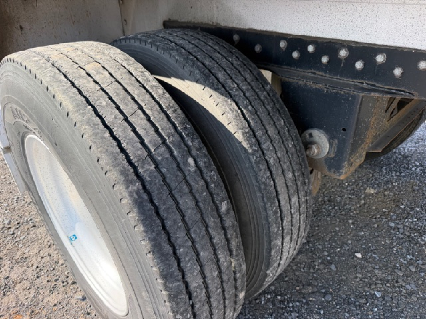 Reitnouer MaxMiser trailer wheel and dual tires showing suspension and frame with gravel surface.