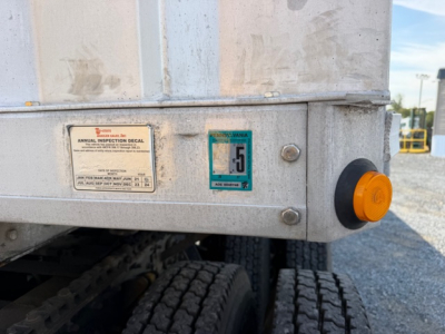Trailer rear corner showing inspection stickers and orange safety marker on a flatbed trailer with dual tires.