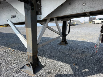 Trailer undercarriage with leveling legs and support beams; metal frame and jack pads visible.