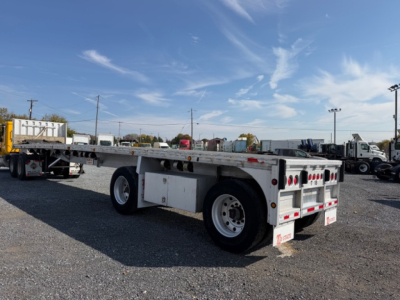 Trailer in a lot showing flatbed with dual rear axles, white sides, storage boxes, and Ramp/kingpins area visible.