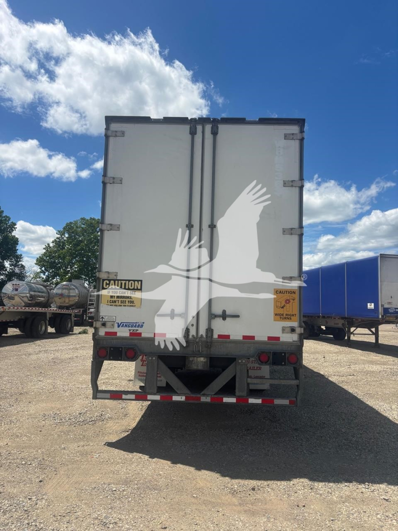 Rear view of a Vanguard trailer with double doors, CAUTION decals, and reflective tape on bumper.