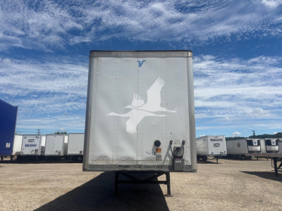 Rear view of a Vanguard trailer showing a large white bird logo on the back doors, blue 'V' at top, and taillights with hitch below.
