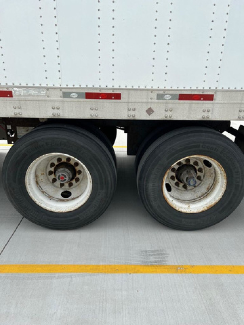Trailer axle and wheels with dual rear tires visible under a utility van trailer.