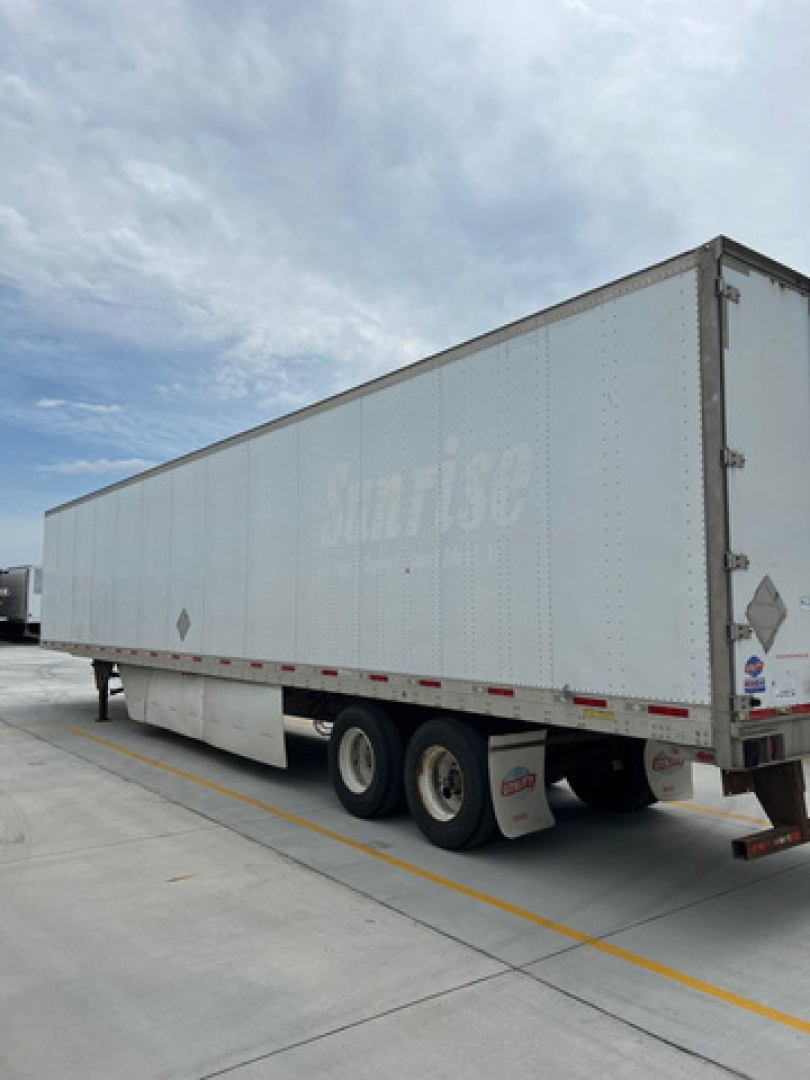 Trailer side view showing a large white utility van trailer with three axles and the word 'Rhino' faded on the side.