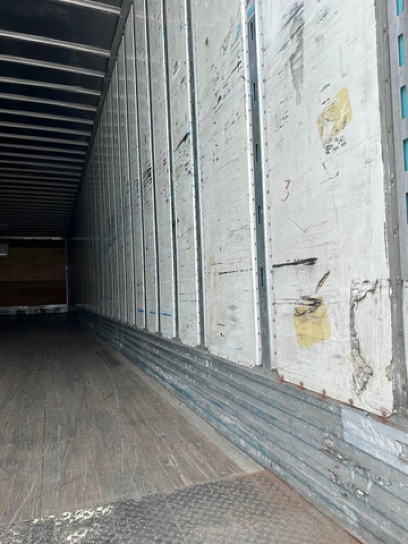Trailer interior showing metal side walls with vertical seams and a textured wooden floor; long, empty cargo area.