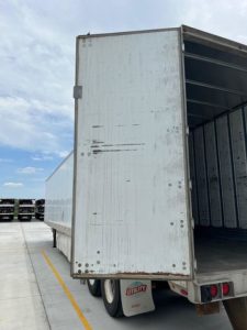 Utility van trailer back door and interior showing open rear with metal walls and raised floor, white exterior with wear marks