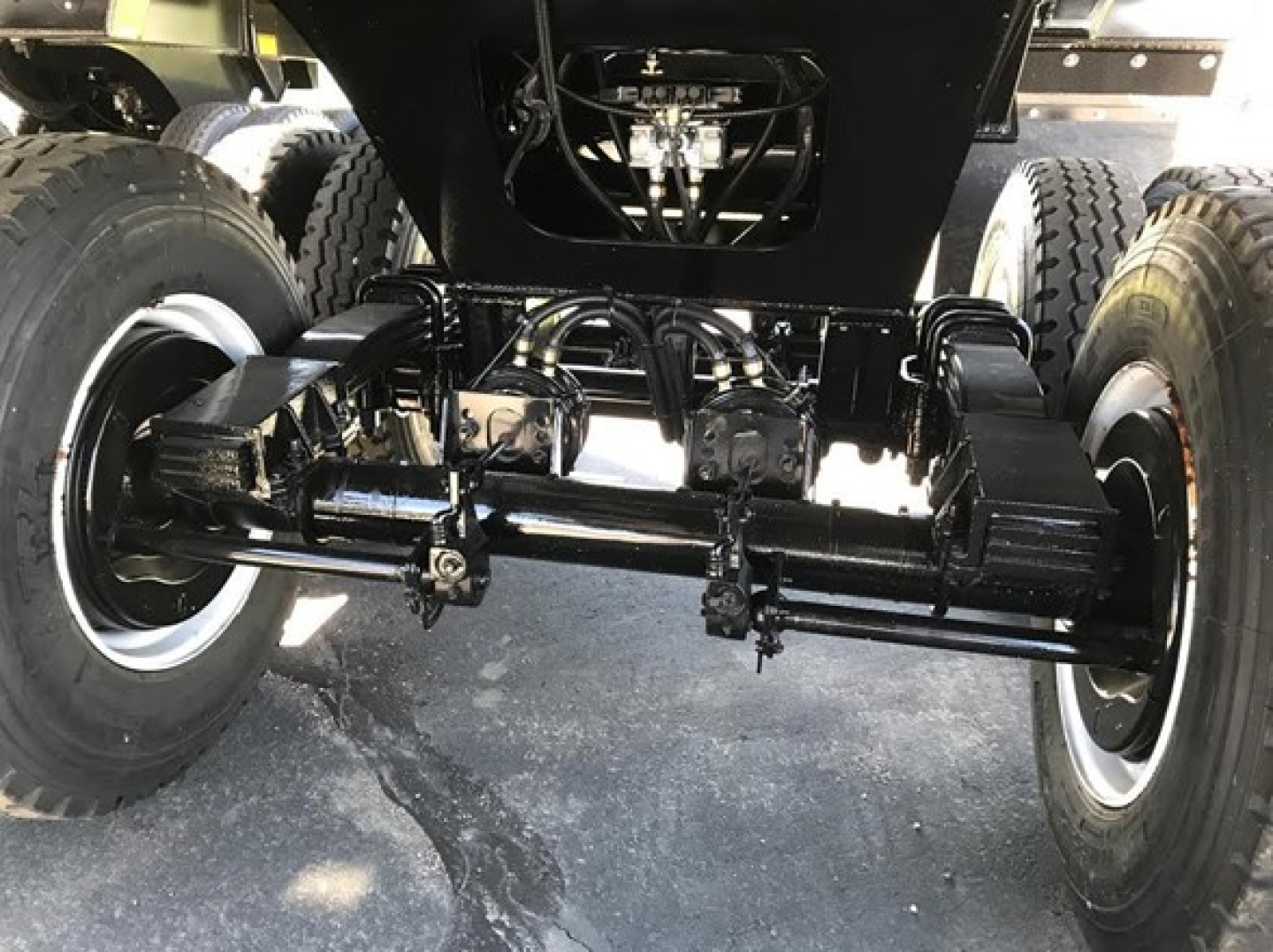 Swivel axle undercarriage of a dump trailer with heavy-duty black-painted steel frame, dual wheels on each side, and hydraulic components visible.