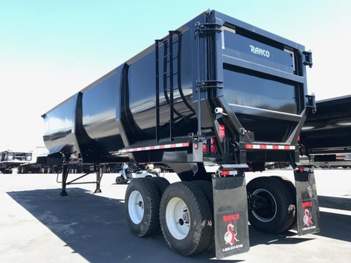 Ranco Ed60-38 dump trailer with black glossy finish, dual rear tires, and rear ramp. Visible text includes RANCO on the back gate.