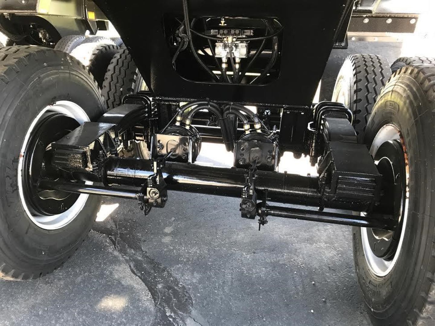 Ranco Ed60-38 trailer undercarriage showing solid heavy-duty axles, leaf springs, and hydraulic lines mounted between dual wheels.