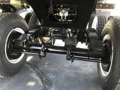 Swivel axle undercarriage of a dump trailer with heavy-duty black-painted steel frame, dual wheels on each side, and hydraulic components visible.