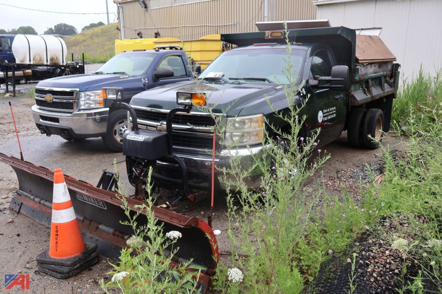 2008 Chevrolet Silverado 3500HD dump truck with plow and sander in a yard, dark color body, front grille guard, snow plow attachment, and vegetation in foreground