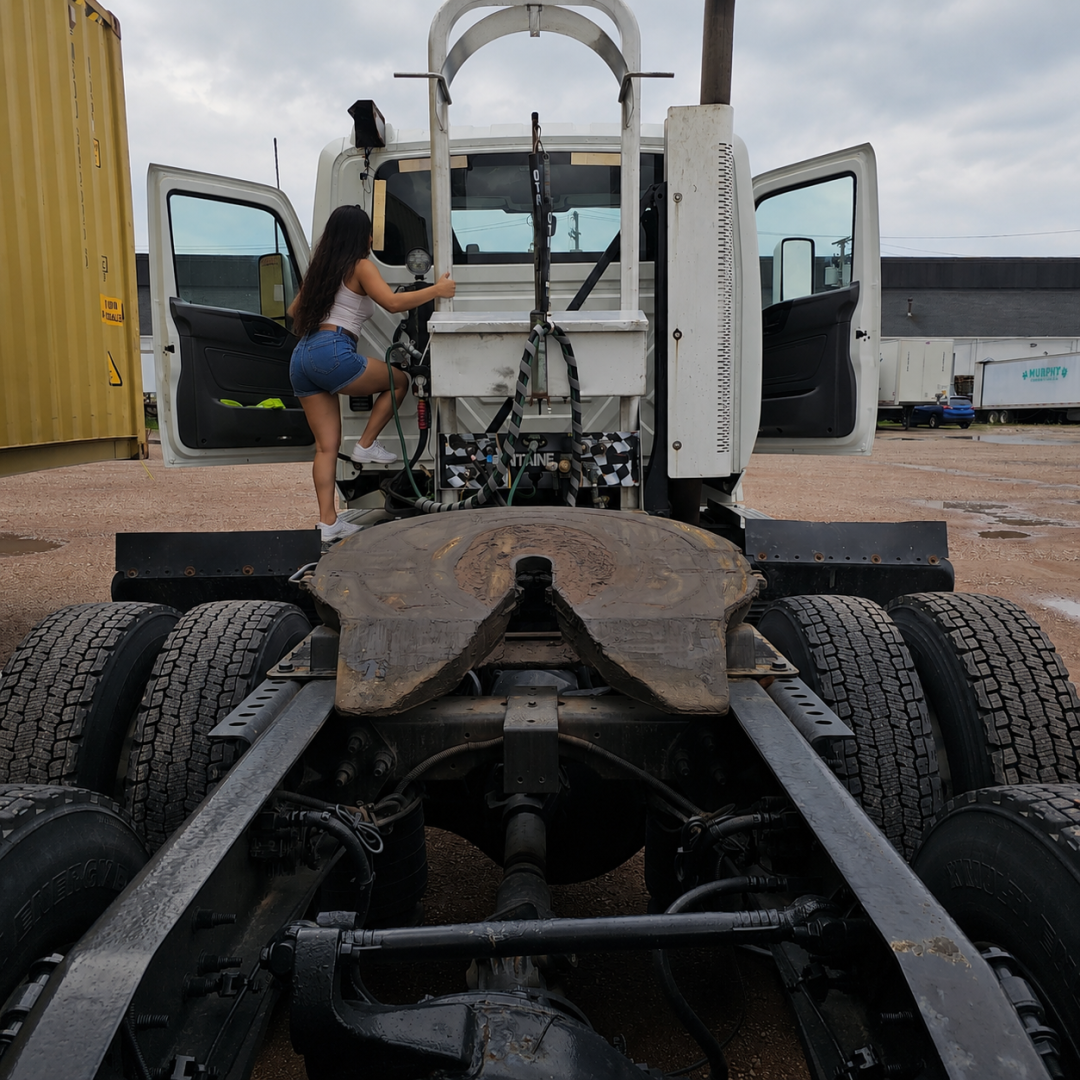 Truck chassis and cab rear view showing exposed drivetrain and open doors, with a person climbing into the cab, 2020 International LT.