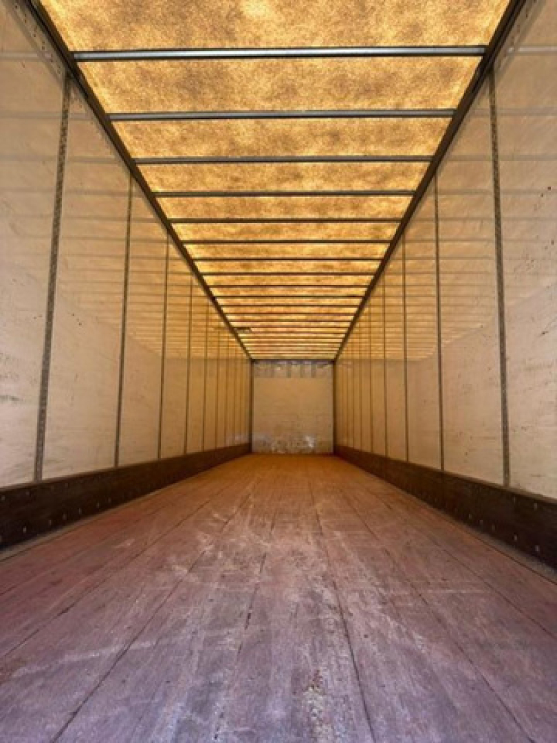 Trailer interior showing long empty cargo area with wooden floor and metal sidewalls, viewed from the back toward the cab.