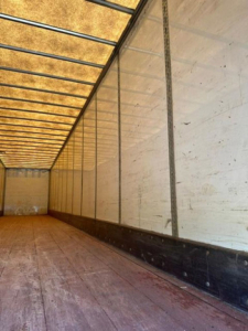 Trailer interior showing long wooden floor and white sidewalls with vertical support posts.