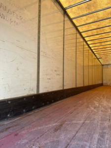 Interior of a used Wabash van trailer with wooden floor and metal side walls; some writing on the left wall reads ‘ANSWER …’ and ‘ONLE!’ visible. Long interior perspective shows roof framing and sidelining.