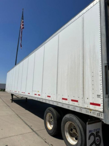 Van trailer side view showing silver Wabash box with white exterior, dual rear wheels, and red reflective tape along lower edge.