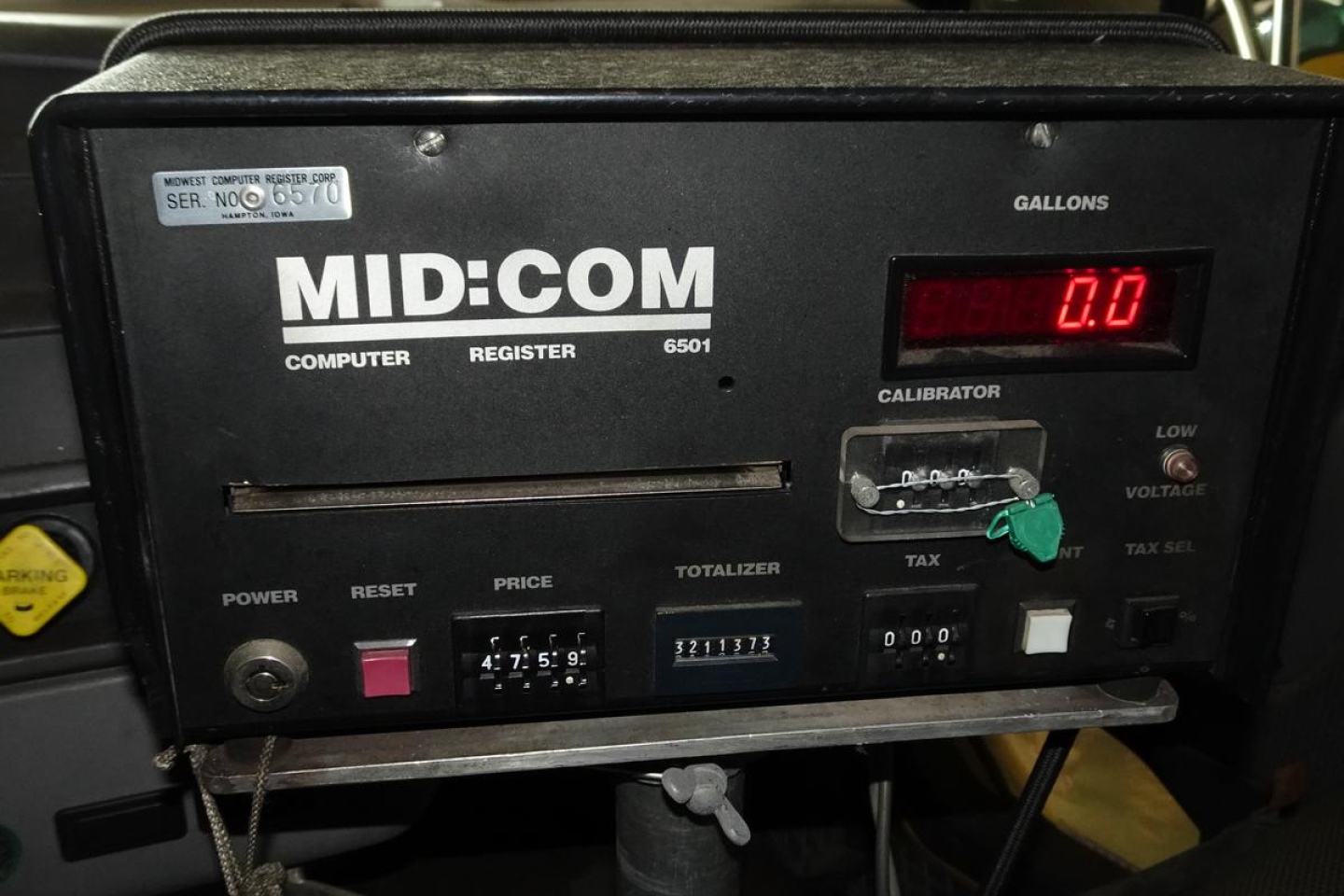 Mid-com computer register panel with MID:COM branding, digital gauge showing 0.0 gallons, and control buttons labeled POWER, RESET, PRICE, TOTALIZER.