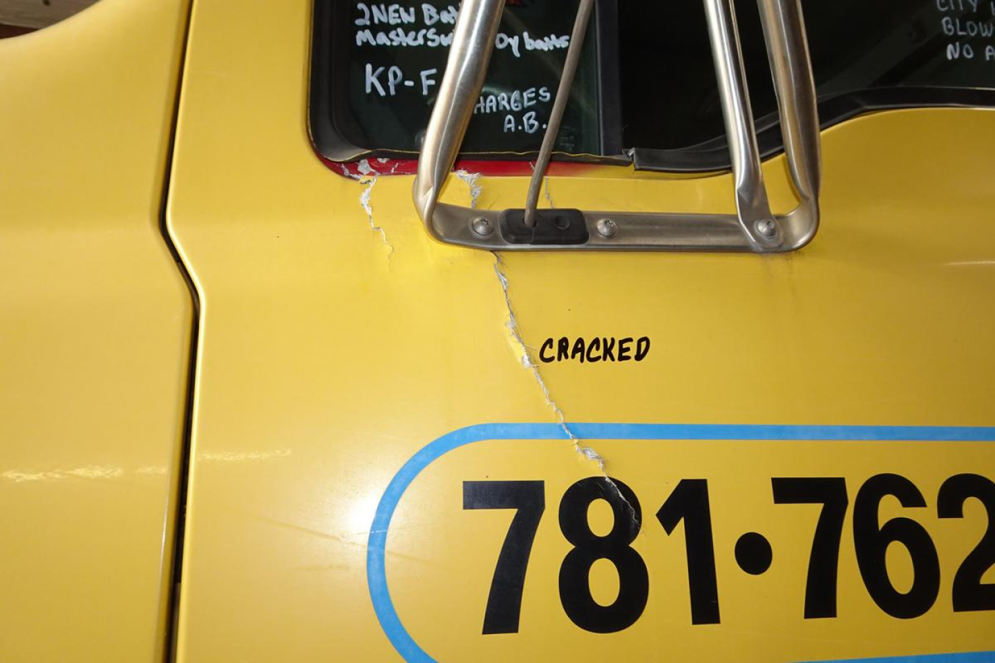 Truck cab side showing cracked door panel with yellow paint and blue numbering 781-762; word 'CRACKED' above the crack and window mirror support visible.