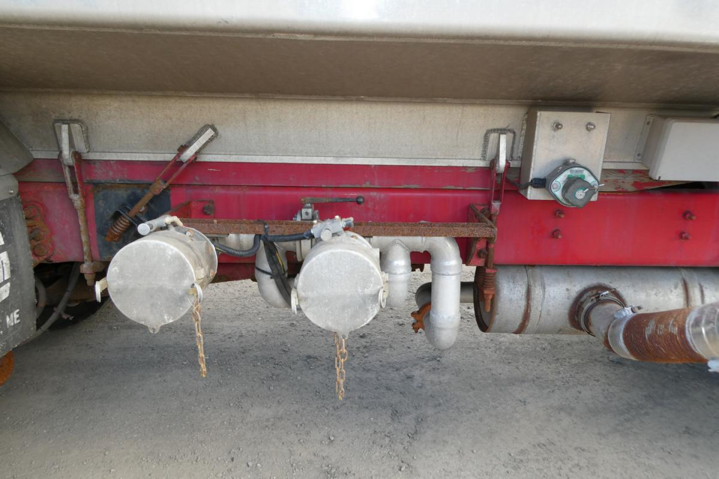 Truck undercarriage showing fuel lines and exhaust components with circular silver containers and piping near rear axle.