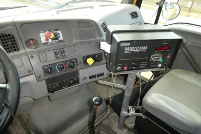 Inside cab of 1999 Sterling L7500 showing dashboard, steering wheel, controls, and a MID-COM generator mounted on a stand near the passenger seat.