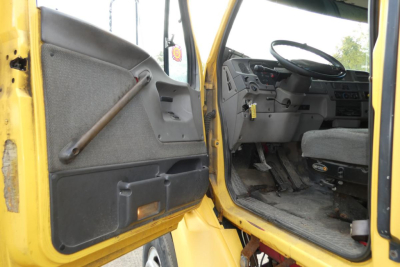 Interior of a yellow Sterling L7500 truck cab with open door, showing steering wheel, instrument panel, and floor; driver’s seat and door panel visible.