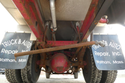 Underbody view of a 1999 Sterling L7500 rear axle and suspension with dual rear wheels, red differential housing, control arms, and mud flaps reading Truck & Auto Repair Inc., Waltham, Mass.