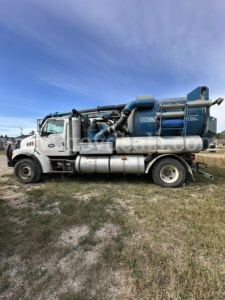 Sterling L7501 vacuum truck side view showing large blue vacuum tank and silver fuel tanks with cab in foreground