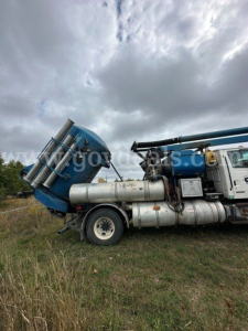 Sterling L7501 vacuum truck side view showing blue cab and large cylindrical tanks with mounted hoses and metal steps.