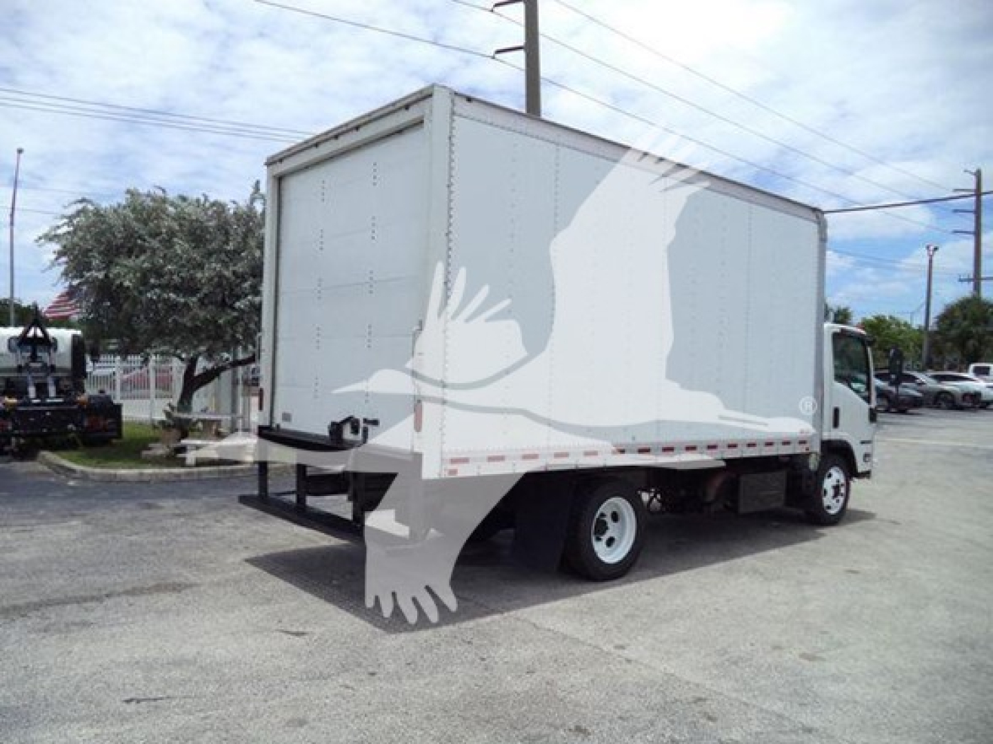 Isuzu NRR box truck from rear three-quarter view with a white cargo box. The image shows a tall box with a cab at right, and a silhouette watermark across the box.