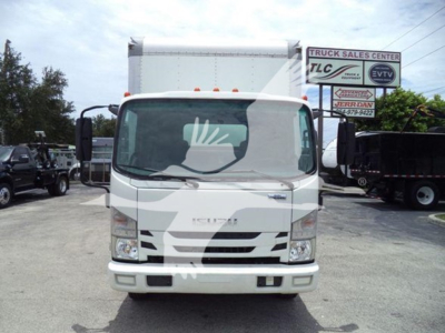 Isuzu NRR box truck front view with stock signs in background. Visible text includes 'ISUZU' on grille and some signs on right side of lot. No other legible model or specification text clearly readable in the image.