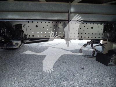 Isuzu truck chassis undercarriage showing perforated frame rails and wiring harness near ground.