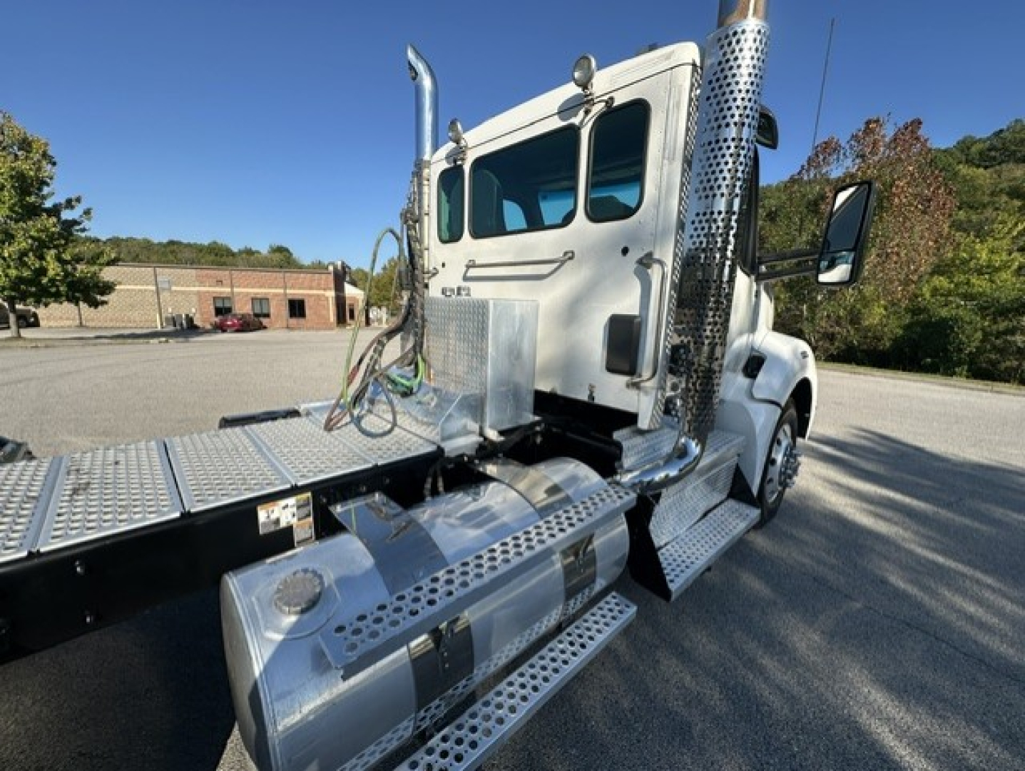 Kenworth T880 conventional daycab truck side view showing aluminum steps and fuel tanks with perforated metal surface.
