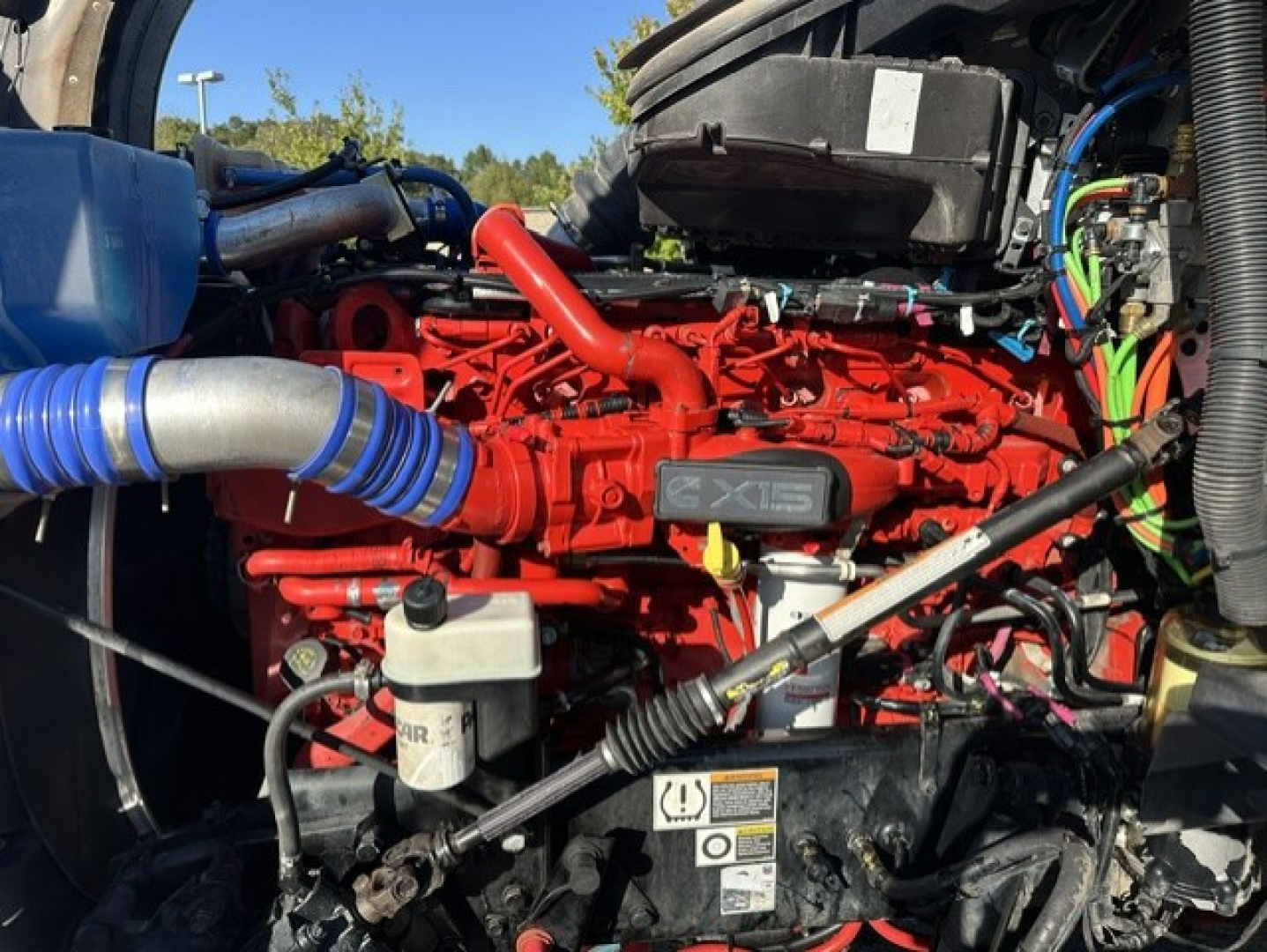 Kenworth T880 engine bay with bright red Cummins X15 engine and blue intake hose, various wires and hoses visible.