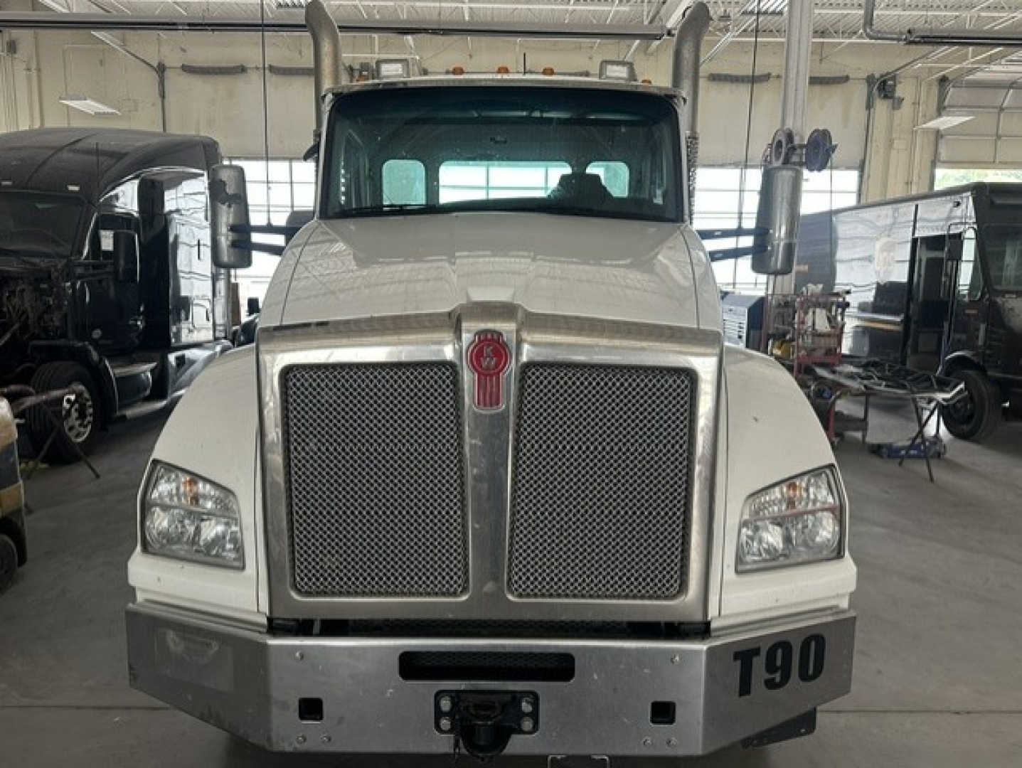 Kenworth T880 front view showing large chrome grille and bumper in a workshop setting.