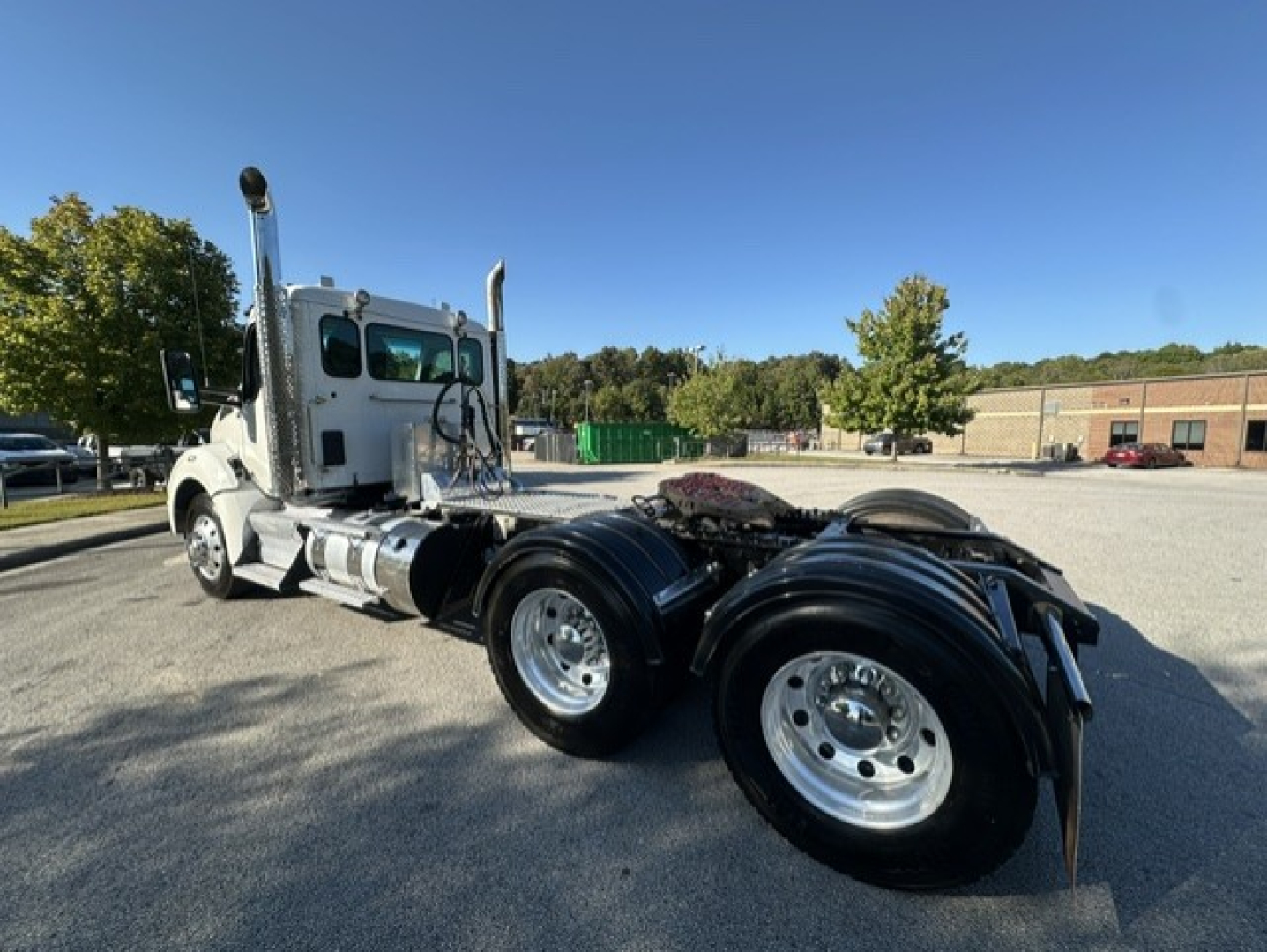 Kenworth T880 tractor chassis view showing rear dual axle tires and cab in left foreground, with clear sky and storage yard in background.