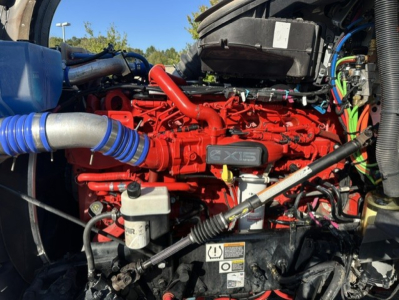 Kenworth T880 engine bay with bright red Cummins X15 engine and blue intake hose, various wires and hoses visible.